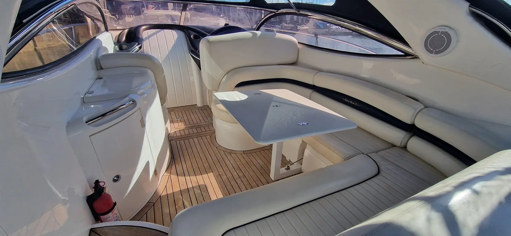 Interior of a luxury boat featuring white leather seating, a small table, and a wooden floor, with a scenic view outside.